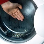 The hand is placed on the glass of the loading hatch of the washing machine.